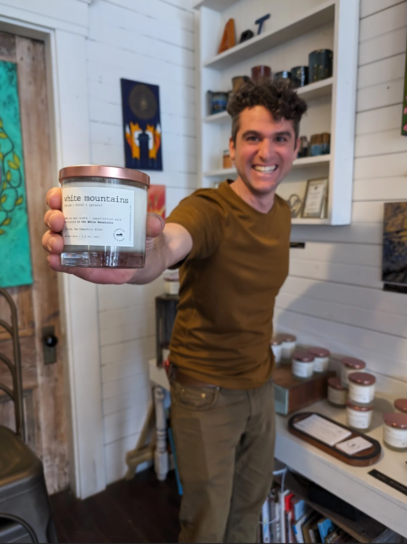 Ben Poirier, who owns River & Stone Candle Co., is one of the artists showcasing work at Three Sisters Gallery in Gorham. (Here, he holds a "White Mountain" scented candle with an enthusiastic smiles on his face.) Poirier crafts his candles to reflect experiences he had growing up or nearby areas that people may love. He said he realizes that everyone has particular associations for different aromas, so he's curious about what people recall or experience as they breathe in.