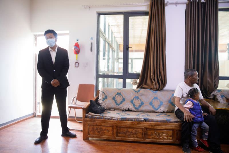 A government official stands in the room as a journalist interviews Tibetan man Rimar who has been relocated from a high-alitude location to a purpose built village in Gongga County