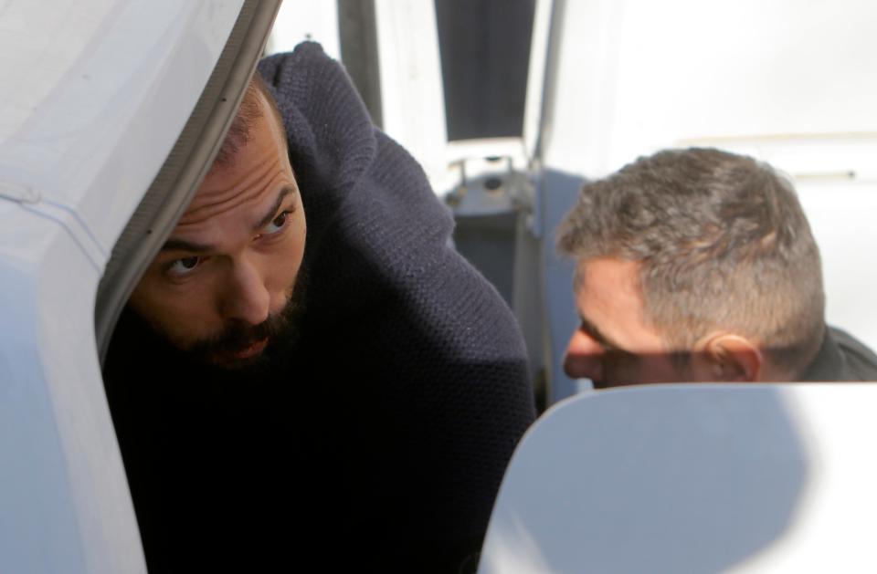 Andrew Tate is escorted into a police car after today’s hearing (EPA)