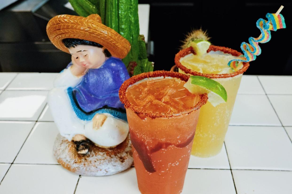 A Michelada, a cucumber version, and a statue of a boy sleeping against a cactus all on the white tile bar of the cantina