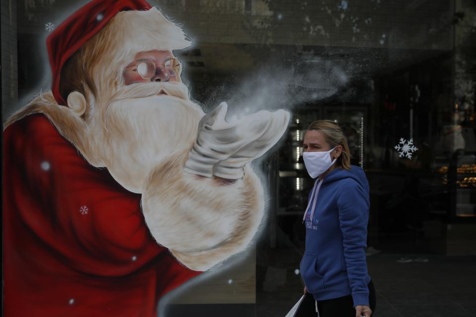 A woman wearing a face mask against the spread of coronavirus, passes a Santa Claus mural by artist Solonas which decorated the store window of a bakery in Athens, Tuesday, Nov. 24, 2020. Greece is set to extend its lockdown measures beyond the end of November given the spread of COVID-19 and the pressure on hospitals, the country's health minister warned Monday. (AP Photo/Thanassis Stavrakis)