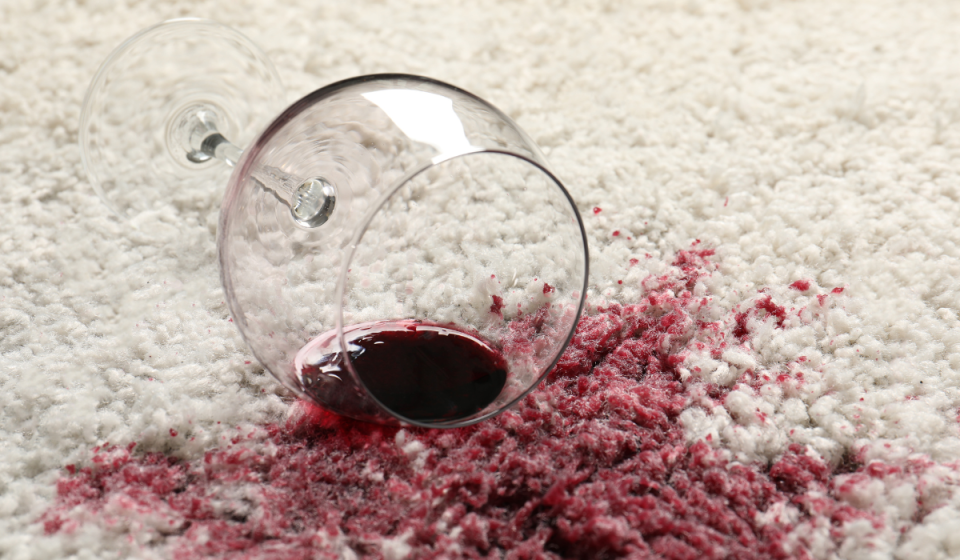 glass of red wine spilled on a white carpet that could benefit from a stain remover