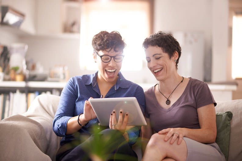 A couple smiles excitedly at their laptop screen in their living room.