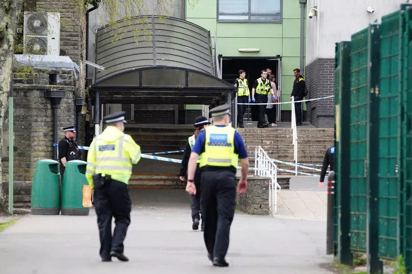 Several police officers walk towards the cordoned-off area in the school as others stand guard and more exit the school building