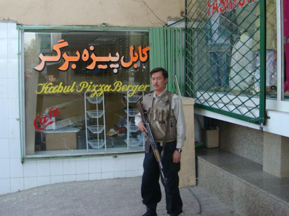 A man with a rifle stands in front of a restaurant window