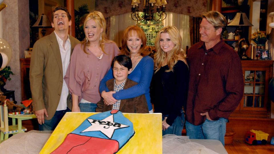 reba cast members cutting into a large cake in celebration of 100 episodes