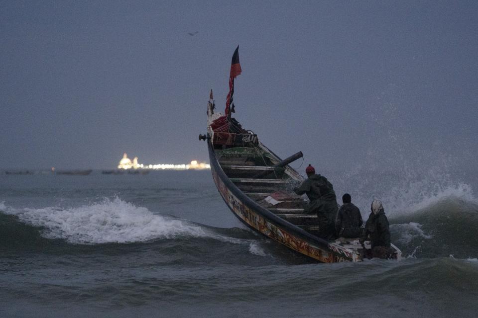 Fishermen on a traditional boat known as pirogue leap over a wave heading out to the Atlantic Ocean as an offshore gas terminal is seen at the horizon in Saint Louis, Senegal, Wednesday, Jan. 18, 2023. The rig was the final straw for Saint-Louis, pushing it to the brink of economic disaster, according to locals, officials and advocates. (AP Photo/Leo Correa)