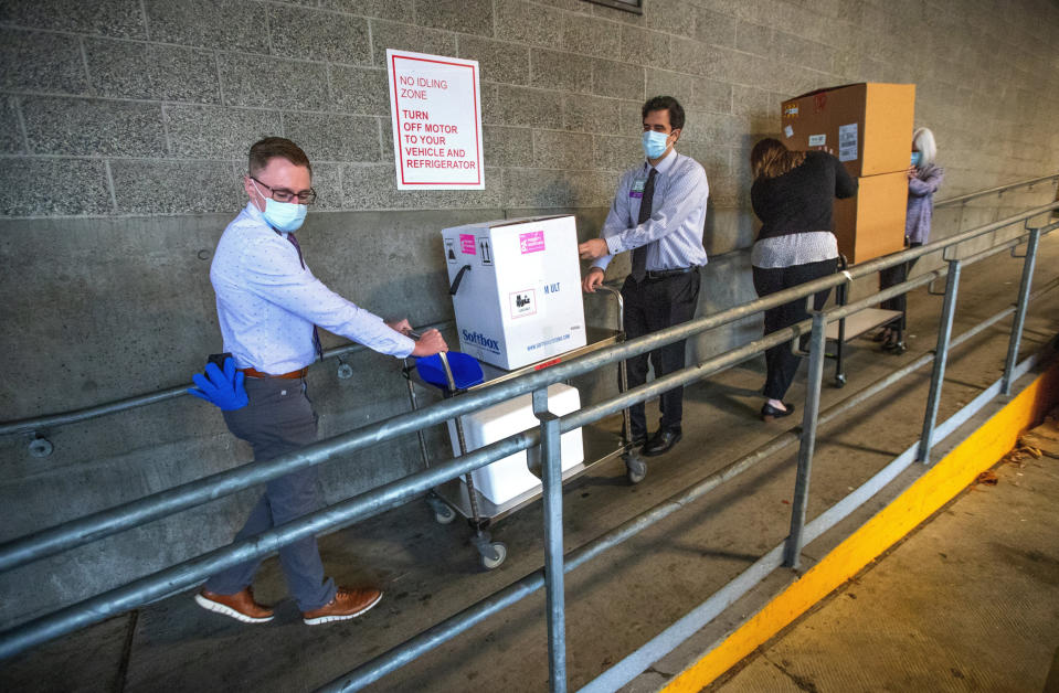 FILE - In this Dec. 14, 2020, file photo, University of Washington Medical Center Montlake campus pharmacy administration resident Derek Pohlmeyer, left, and UWMC pharmacy director Michael Alwan transport a box containing Pfizer-BioNTech COVID-19 vaccines toward a waiting vehicle headed to the UW Medical Center's other hospital campuses in Seattle. (Mike Siegel/The Seattle Times via AP, Pool, File)