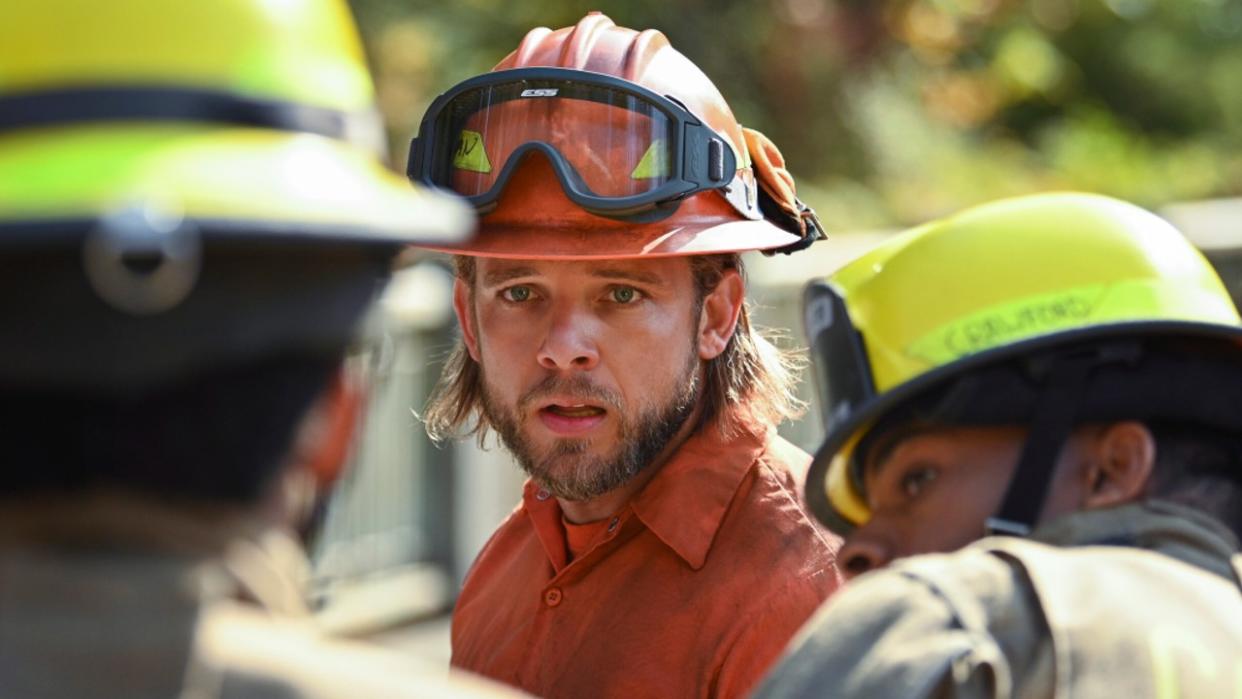  Max Thieriot looking into the distance with two other firefighters in the foreground on Fire Country. 