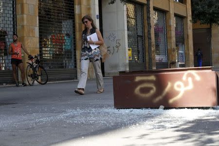 A woman walks near shattered glass as the word "revolution" is seen on a broken advertising billboard in downtown Beirut, Lebanon August 24, 2015.REUTERS/Jamal Saidi