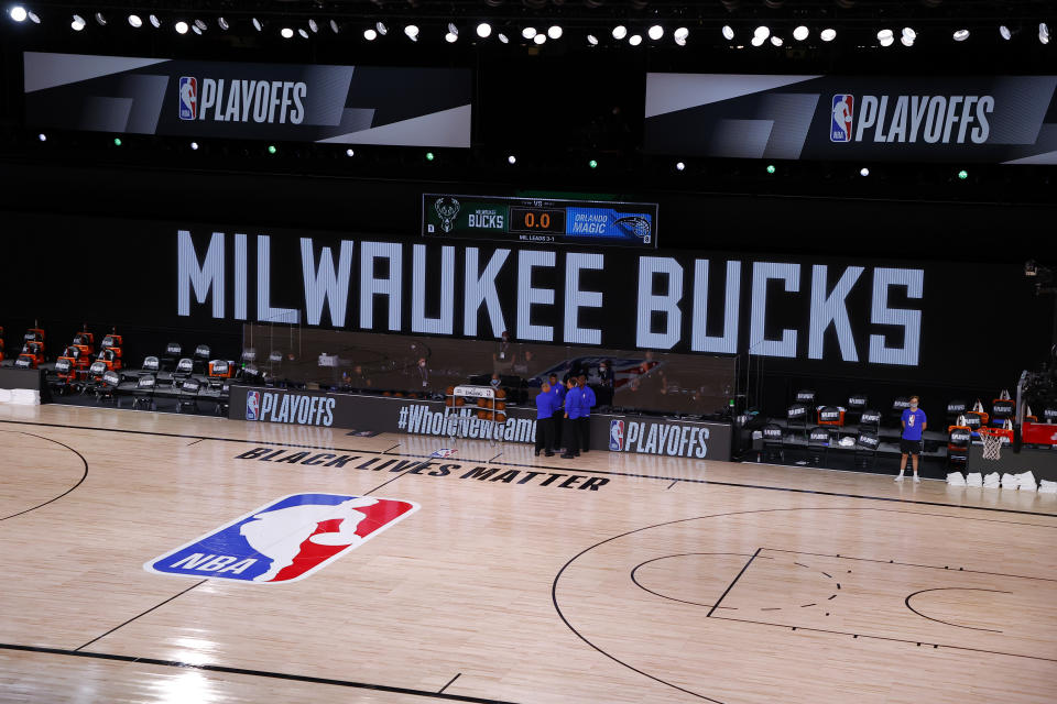 Referees huddle on an empty court at game time of a scheduled game between the Milwaukee Bucks and the Orlando Magic for Game 5 of an NBA basketball first-round playoff series, Wednesday, Aug. 26, 2020, in Lake Buena Vista, Fla. (Kevin C. Cox/Pool Photo via AP)