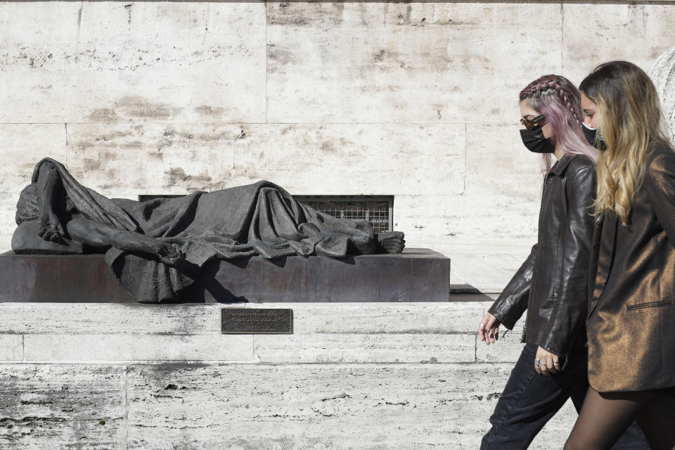 Girls wearing face masks walk past a sculpture by Canadian Artist Timothy Schmalz outside Santo Spirito hospital in Rome, Sunday, Oct. 18, 2020. The number of confirmed positive cases of coronavirus in Italy continued to rise to new records, hitting 11,705 in the last 24 hours. (AP Photo/Gregorio Borgia)