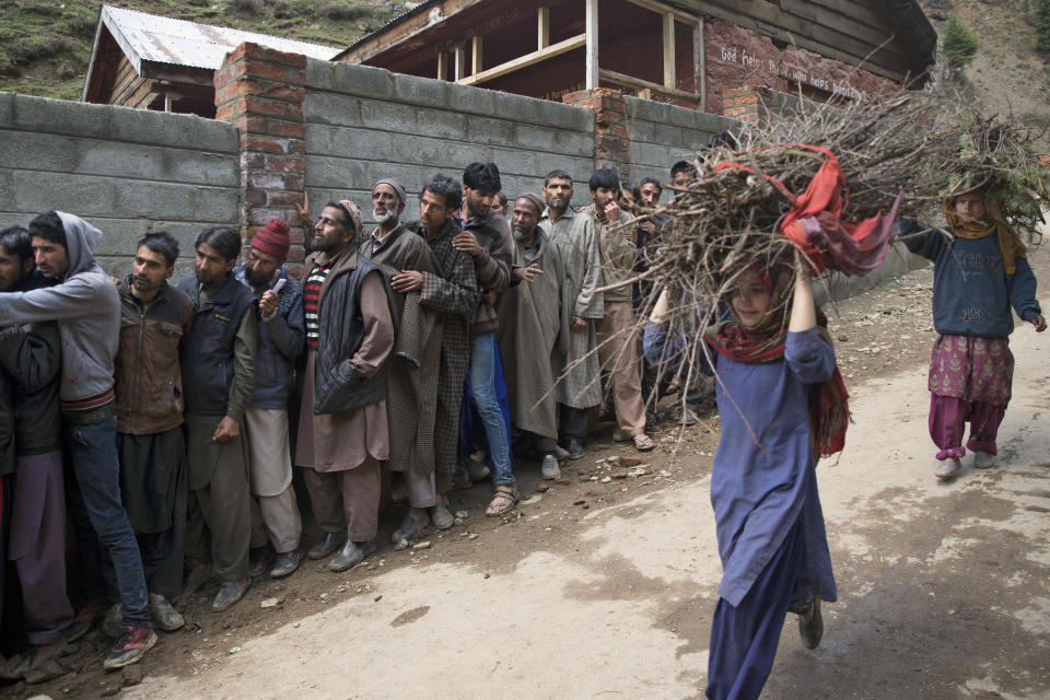 Young Kashmiri girls carry firewood and walk past voters standing in a queue outside a polling station during the second phase of India's general elections, in Baba Nagri, about 44 kilometers (28 miles) northeast of Srinagar, Indian controlled Kashmir, Thursday, April 18, 2019. Kashmiri separatist leaders who challenge India's sovereignty over the disputed region have called for a boycott of the vote. Most polling stations in Srinagar and Budgam areas of Kashmir looked deserted in the morning with more armed police, paramilitary soldiers and election staff present than voters. (AP Photo/ Dar Yasin)