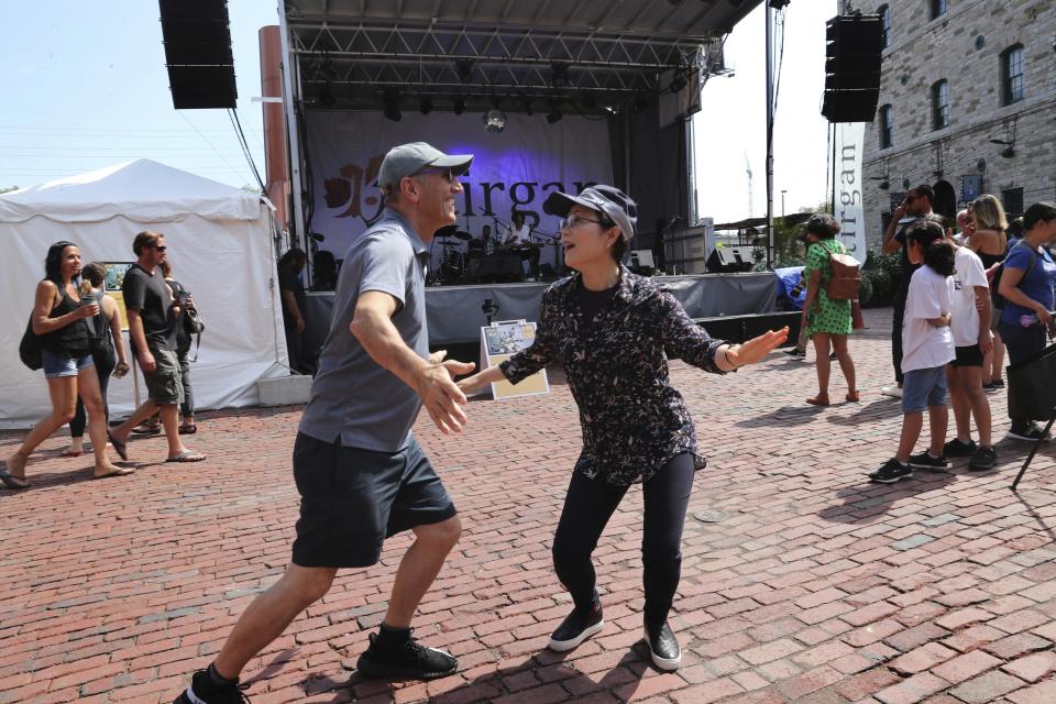 In this Saturday, July 27, 2019 photo, an Iranian man dances with a passerby woman in front of the Tirgan summer festival main stage at the Distillery Historic District in Toronto, Canada. The event aims to preserve and celebrate Iranian and Persian culture, said festival CEO Mehrdad Ariannejad. Among those who attended were second-and third-generation immigrants, many of whom have never been to Iran or have not been there since leaving the country following the 1979 Islamic Revolution. (AP Photo/Kamran Jebreili)