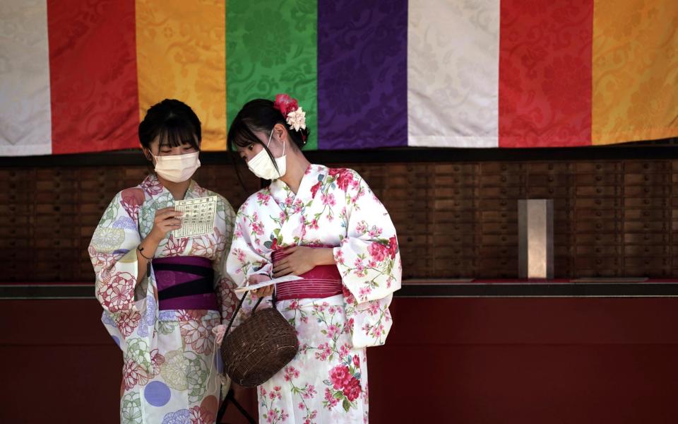 Visitors in yukatas or Japanese traditional summer kimonos wear face masks as they draw a fortune-telling paper strip at the Sensoji Temple in the Asakusa district of Tokyo on 20 September 2021 - Eugene Hoshiko/AP