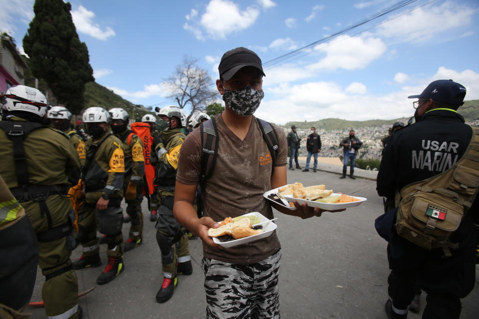 A volunteer offers plates of food to soldiers working in the search and rescue efforts at the site of a landslide that brought tons of massive boulders down on a steep hillside neighborhood, in Tlalnepantla, on the outskirts of Mexico City, Saturday, Sept. 11, 2021. A section of the peak known as Chiquihuite gave way Friday afternoon, plunging rocks the size of small homes onto the densely populated neighborhood. (AP Photo/Ginnette Riquelme)
