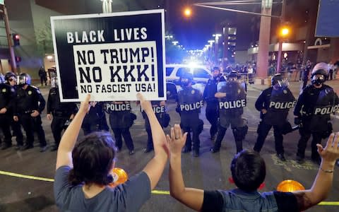 Protesters raise their hands after Phoenix police used tear gas outside the Phoenix Convention Centre - Credit: AP