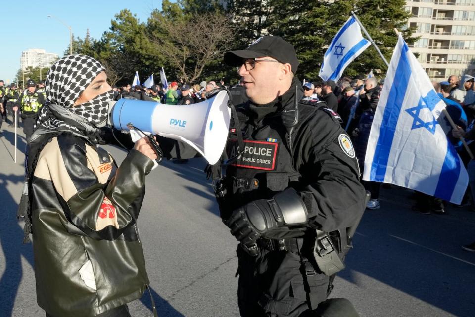 A pro-Palestine protester is confronted by a police officer after breaching a line to walk towards pro-Israel protesters across the street at a demonstration in front of a synagogue hosting 