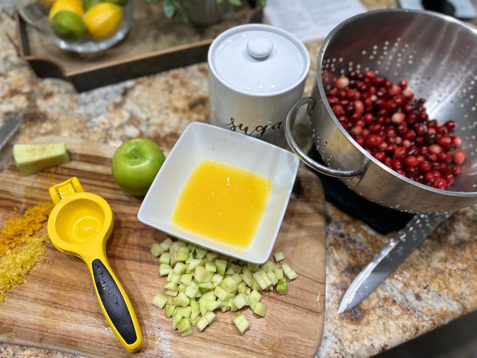 Melted butter, lemon juicer, and strainer full of cranberries on counter