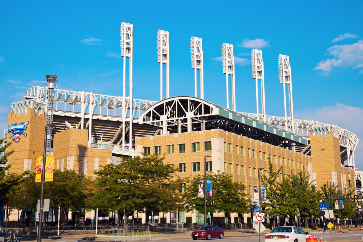 Exterior of Progressive Field, Cleveland, home of the Cleveland Guardians with tree lined sidewalk and road with cars parked