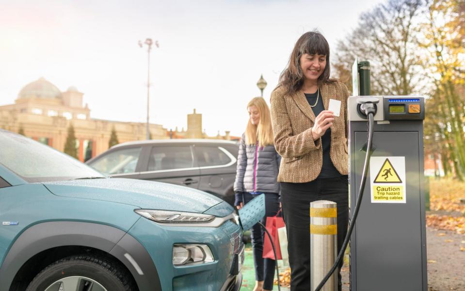 Female shoppers charging electric car at charge point, Manchester, UK - Cultura Creative / Alamy