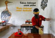 A worker wearing a face shield and a mask wipes a protective screen on a table at a restaurant, in Jakarta