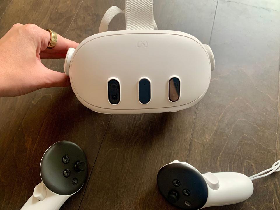 A hand next to an oblong white Meta VR headset with two black-and-white controllers in front of it