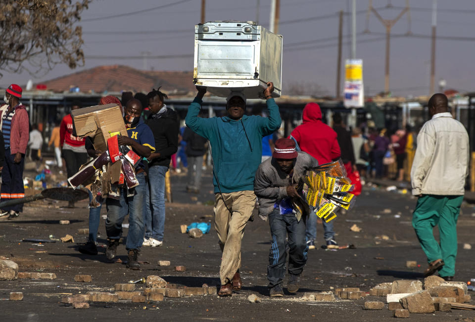 Looters carry items at Letsoho Shopping Centre in Katlehong, east of Johannesburg, South Africa, Monday, July 12, 2021. Police say six people are dead and more than 200 have been arrested amid escalating violence during rioting that broke out following the imprisonment of South Africa's former President Jacob Zuma. (AP Photo/Themba Hadebe)