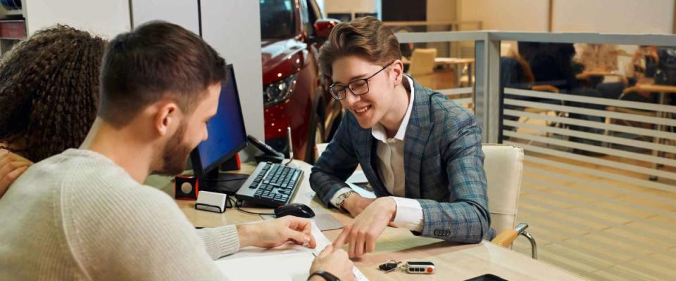 smiling handsome shop assistant explaing the features of luxury car, close up photo. dealer asking family to sign a document. close up photo