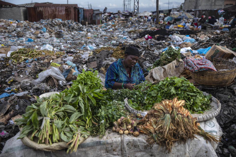 A woman selling greens waits for customers in the Croix des Bosalles market in Port-au-Prince, Haiti, Wednesday, Sept. 22, 2021. The floor of the market is thick with decomposing trash and, in some places, small fires of burning trash. (AP Photo/Rodrigo Abd)