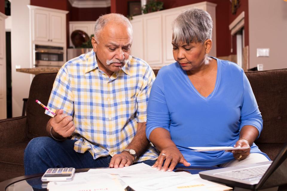 A couple seated on a couch who are examining bills and financial statements set on a table in front of them.