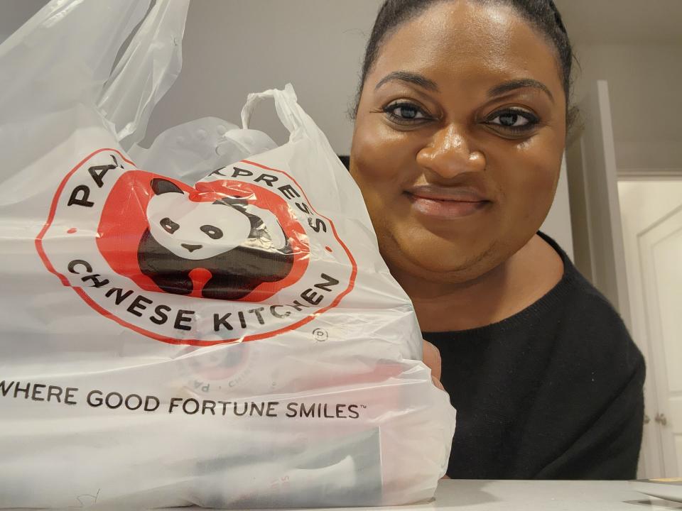 The writer smiles and poses with a Panda Express bag full of food on a counter