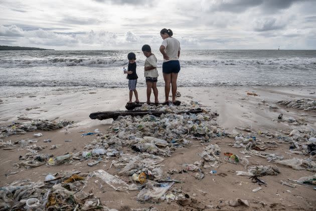 A woman with two boys stand on some wood which is covered by plastic trash at a beach in Bali. (Photo: Agung Parameswara via Getty Images)
