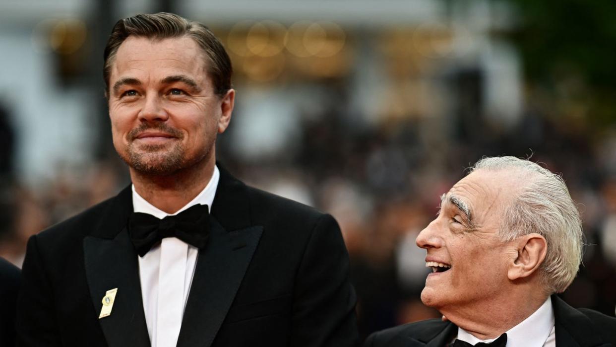 leonardo dicaprio and martin scorsese smiles while wearing black tuxedos, dicaprio looks slightly upward and scorsese looks over at him