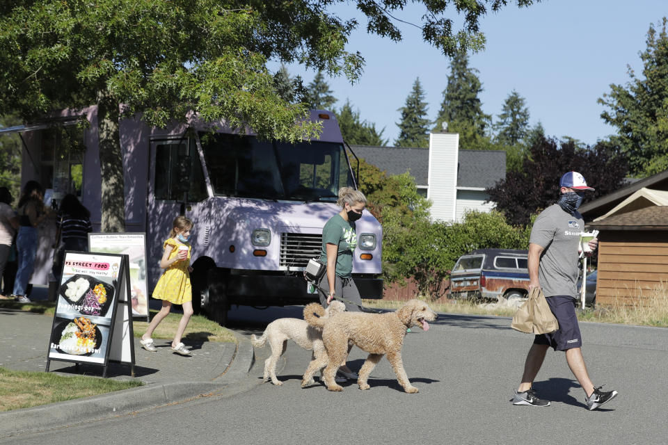 Bobby Price, right, and Catherine Vogt, center, walk with Catherine's daughter Avery, 8, and their dogs after ordering food and drinks from the YS Street Food and Dreamy Drinks food trucks, Monday, Aug. 10, 2020, near the suburb of Lynnwood, Wash., north of Seattle. Long seen as a feature of city living, food trucks are now finding customers in the suburbs during the coronavirus pandemic as people are working and spending most of their time at home. (AP Photo/Ted S. Warren)