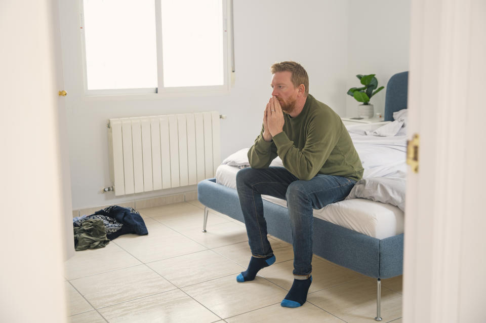 Man sits at the end of a bed and looks stressed. (Getty Images)