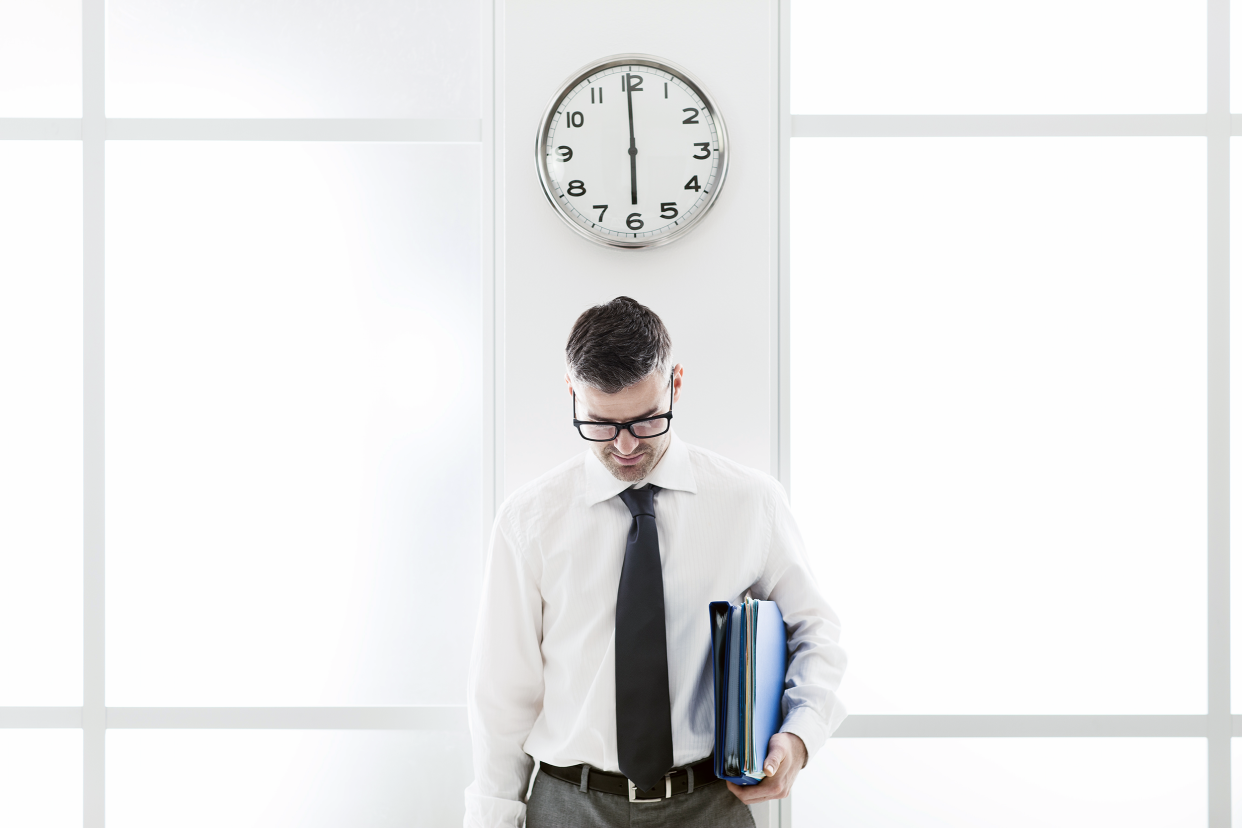 Man standing under a clock in the office and looking down