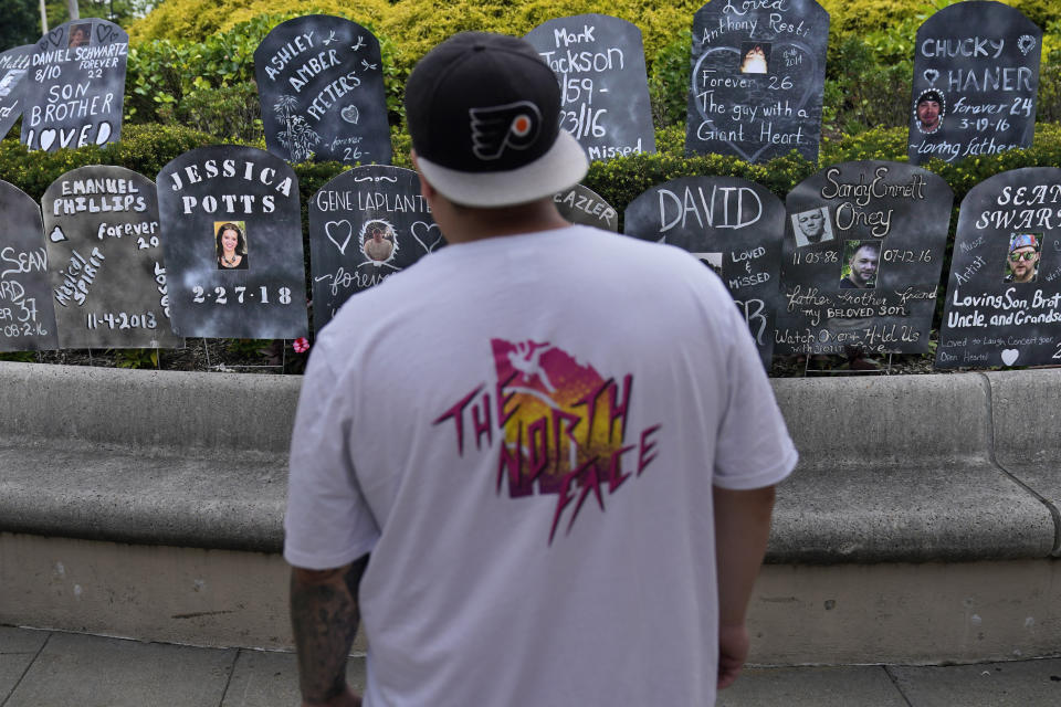 A man looks at cardboard gravestones with the names of victims of opioid abuse outside the courthouse where the Purdue Pharma bankruptcy is taking place in White Plains, N.Y., Monday, Aug. 9, 2021. Purdue Pharma's quest to settle thousands of lawsuits over the toll of OxyContin is entering its final phase with the grudging acceptance of most of those with claims against the company. A confirmation hearing is to open in U.S. Bankruptcy Court on Thursday for a deal that removes control of the company from members of the wealthy Sackler family and requires them to contribute $4.5 billion to opioid abatement While most states and others with claims have signed on, there's still deep anger that Sackler family members would receive protection from lawsuits under the deal. (AP Photo/Seth Wenig)