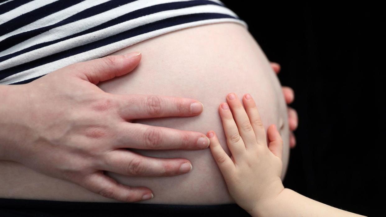  a child placing a hand on the stomach of a pregnant woman, as