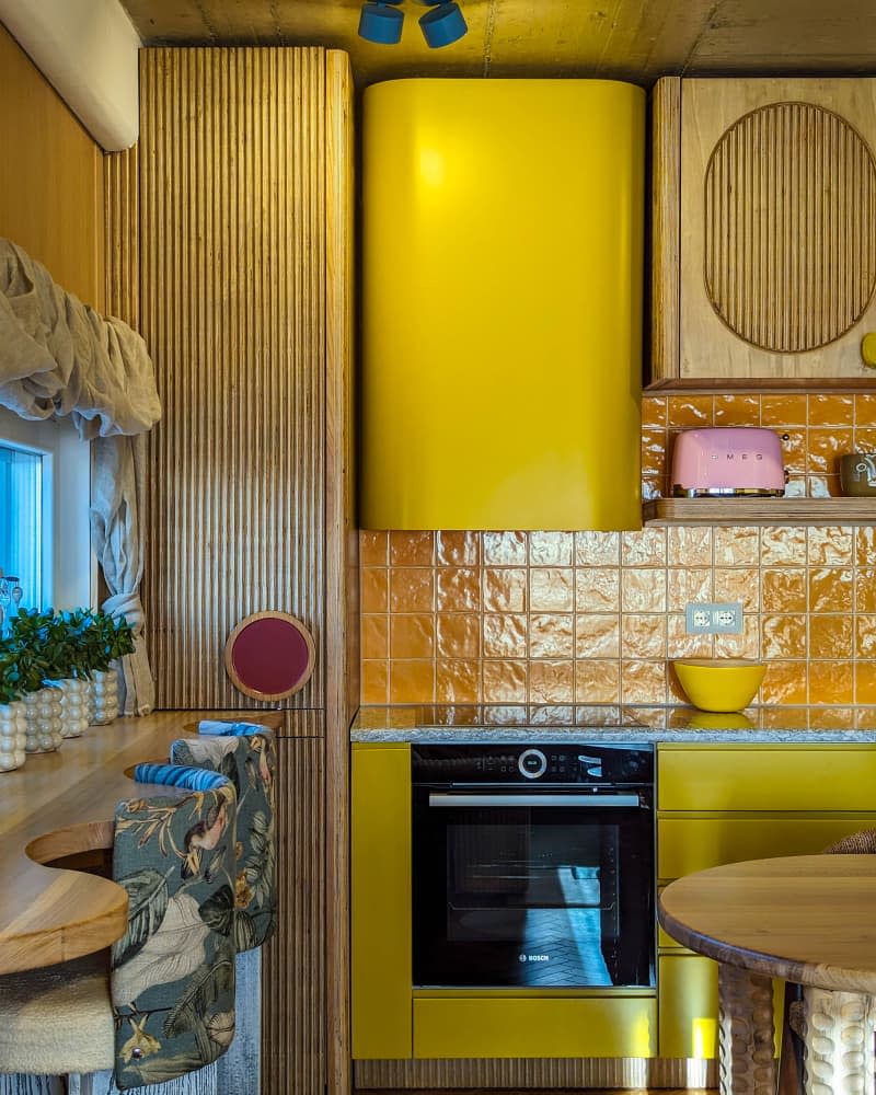 yellow kitchen with wavy wood window counter with botanical fabric backed stools and lots of potted plants