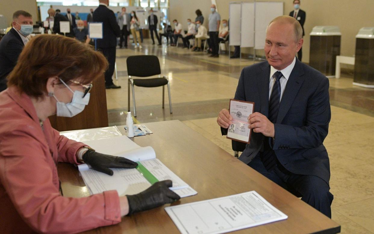 Vladimir Putin shows his ID to an election official before casting his ballot at a polling station in Moscow - Alexei Druzhinin/AFP