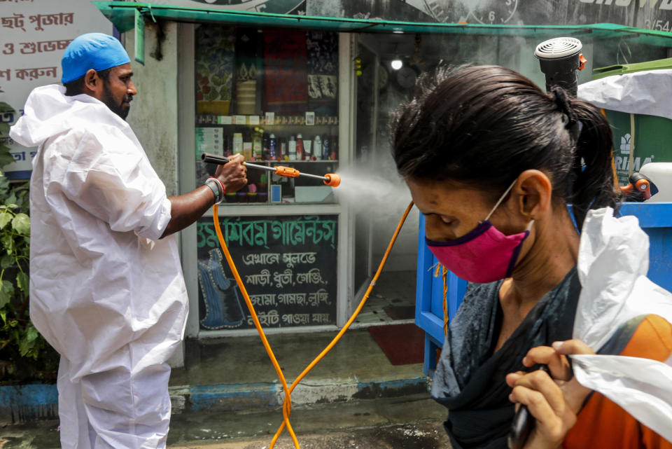 A civic worker sprays sanitizers in front of a shop as a woman wearing face mask walks past in Kolkata, India, Sunday, Aug. 30, 2020. India has the third-highest coronavirus caseload after the United States and Brazil, and the fourth-highest death toll in the world. (AP Photo/Bikas Das)