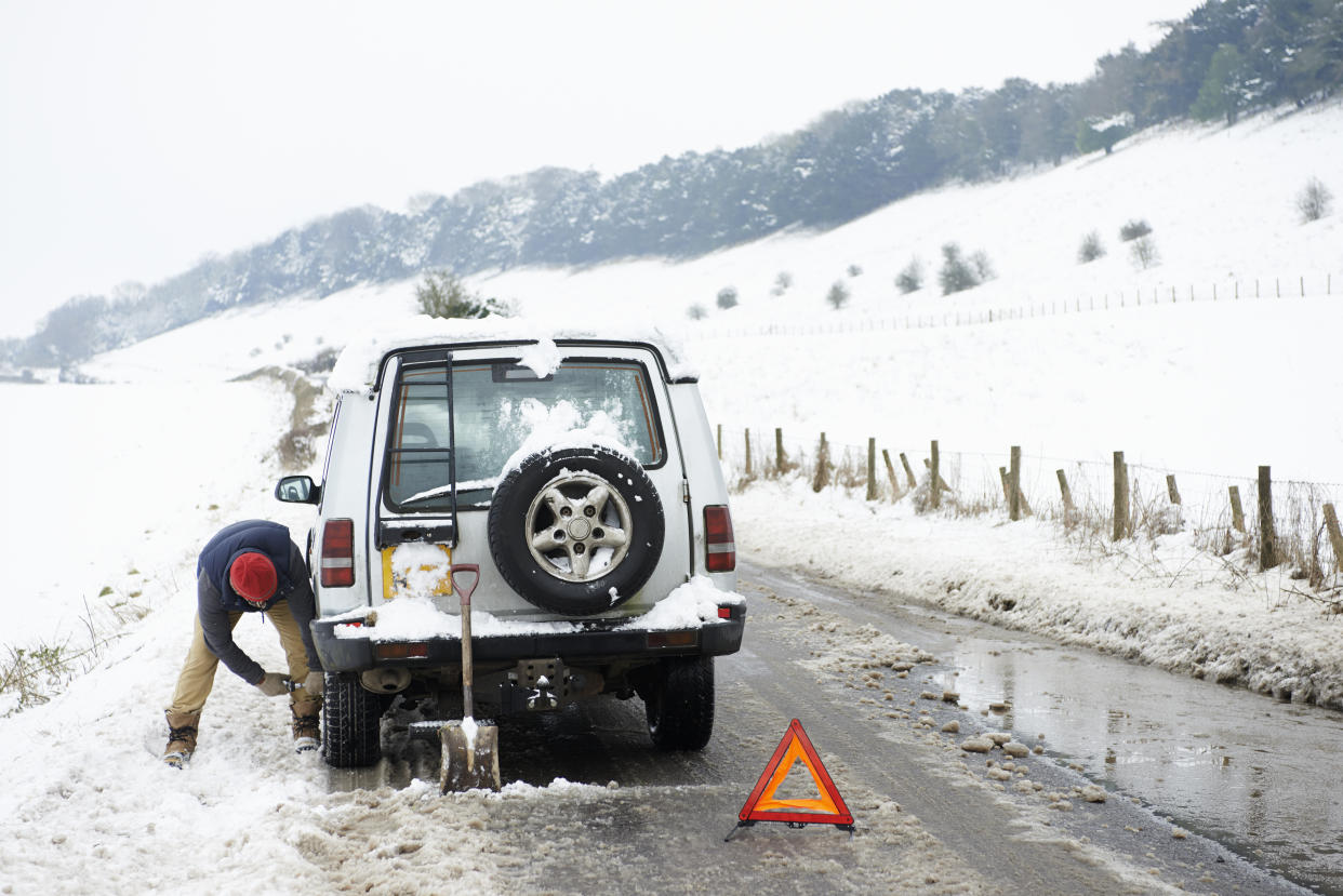 Man working on broken down car in snow/Getty Images