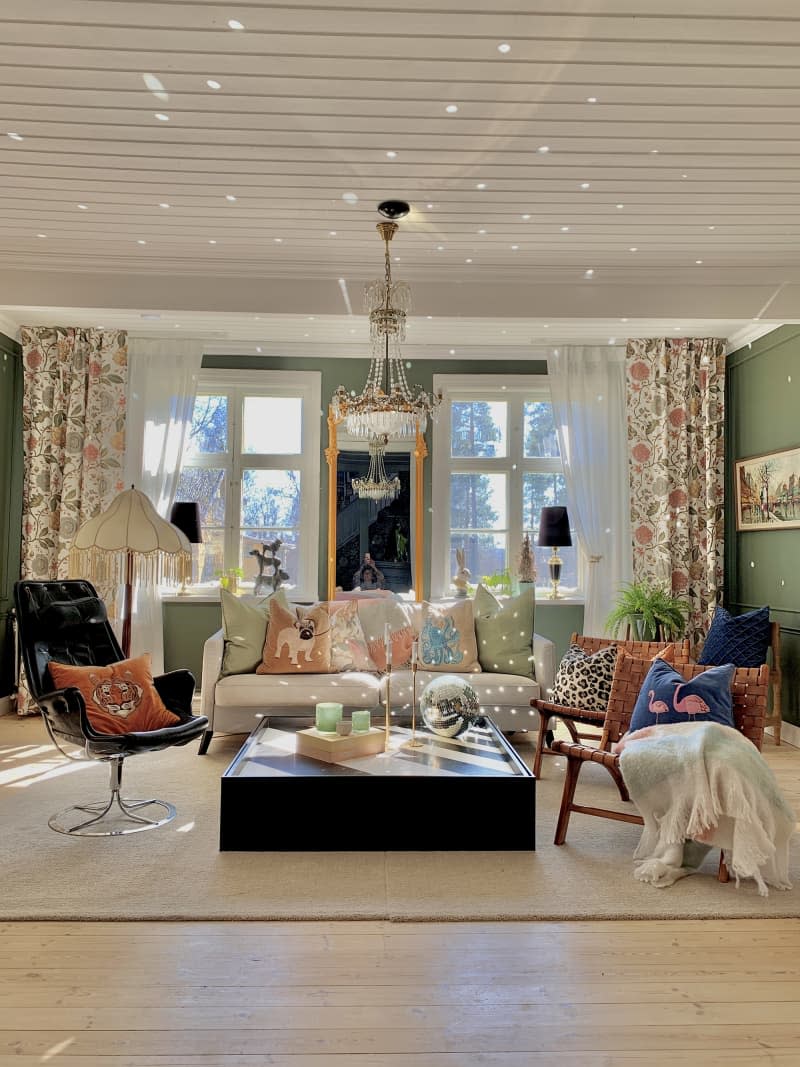 Green eclectic living room with pale gray sofa, crystal chandelier, and colorful vintage accents