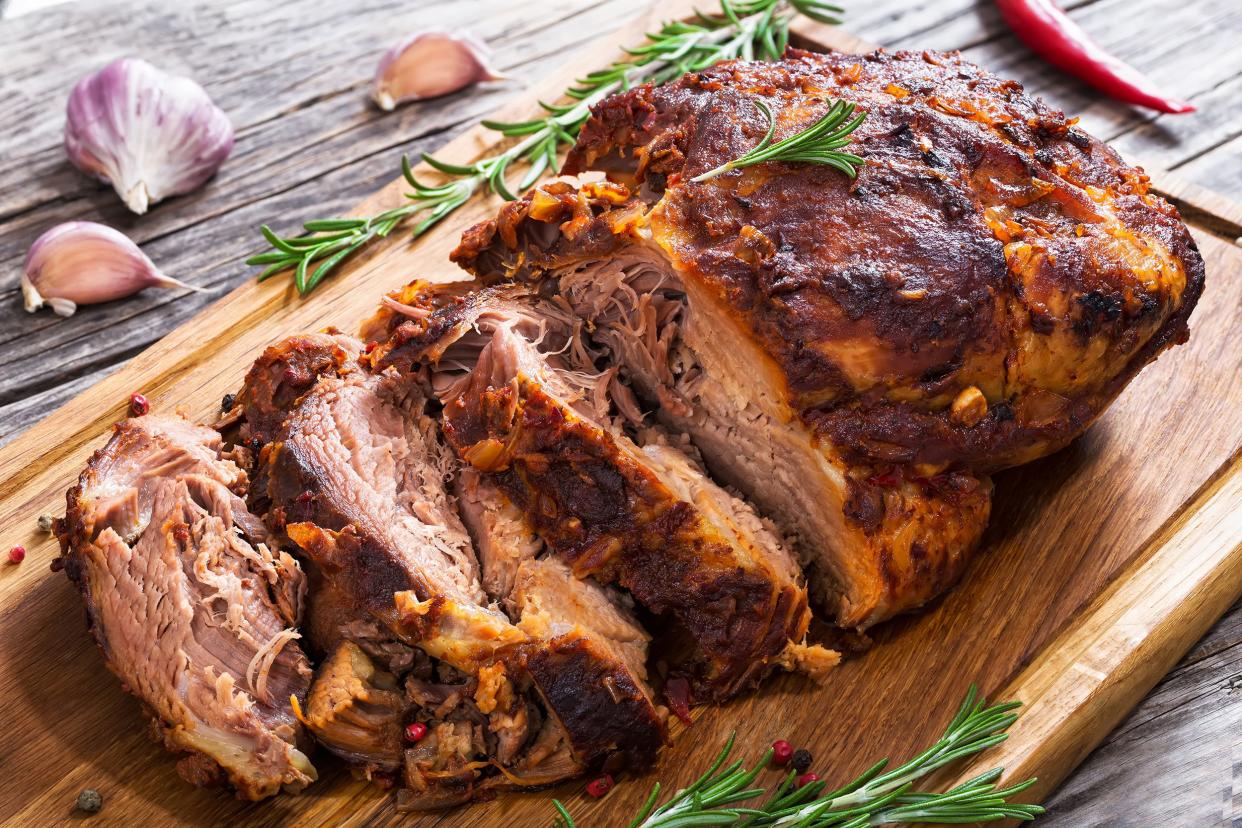 Slow-roasted pork with kumquats on a wooden cutting board with herbs and garlic on a grey wooden table