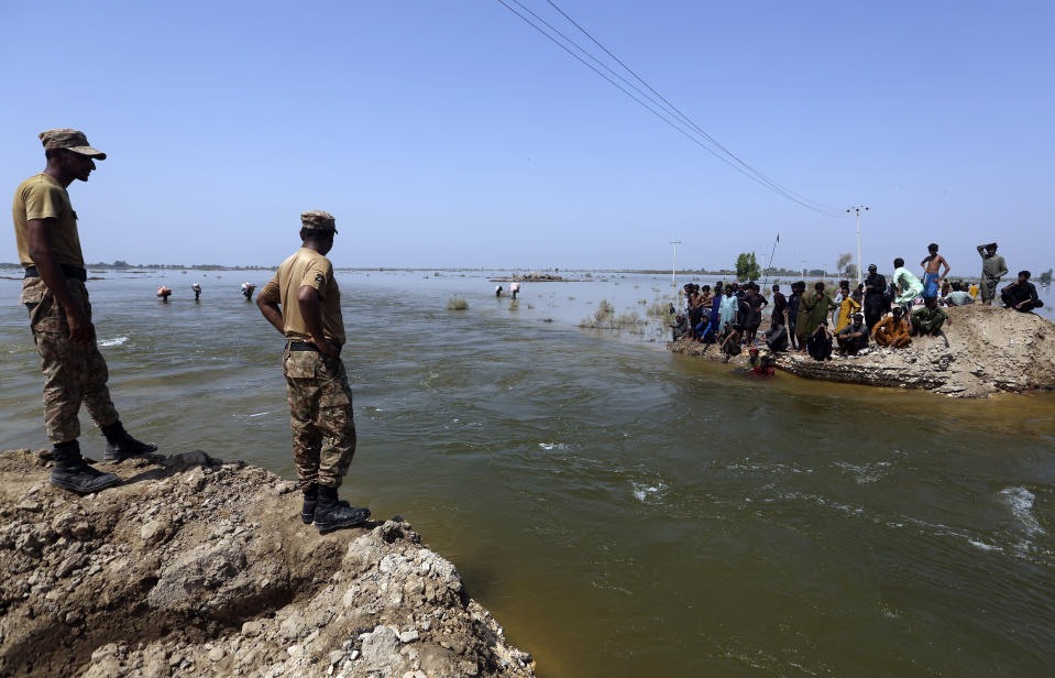 Soldiers survey the flood waters as victims wait to receive relief aid from the Pakistani Army in the Qambar Shahdadkot district of Sindh Province, Pakistan, Friday, Sept. 9, 2022. U.N. Secretary-General Antonio Guterres appealed to the world for help for cash-strapped Pakistan after arriving in the country Friday to see the climate-induced devastation from months of deadly record floods. (AP Photo/Fareed Khan)