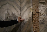 A man indicates salts on the St. Mark's Basilica's inside wall, in Venice, Italy, Thursday, Oct. 7, 2021. Lashing winds that pushed 1.87 meters (nearly 6 feet 2 inches) of water into Venice in November 2019 and ripped the lead tiles off St. Mark's Basilica for the first time ever shocked Venetians with the city's second-worst flood in history, but it was the additional four exceptional floods over the next six weeks that triggered fears about the impact of worsening climate change. (AP Photo/Antonio Calanni)