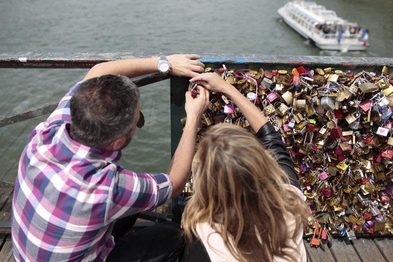 A couple locks a padlock on the "Pont des Arts" on May 29, 2015, in Paris, as the city's municipalty announced that the bridge's fences will be removed due to the weight of the padlocks