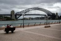 People sit on a bench at the mostly deserted promenade of the Sydney Opera House