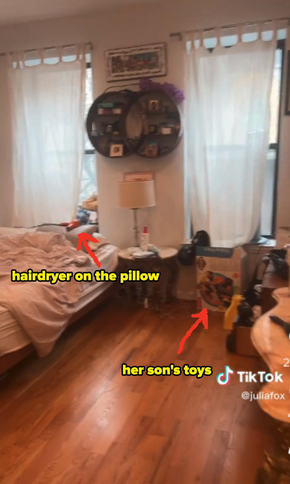 Julia's unmade bed in on the left underneath one of the windows with a hairdryer lying on the pillow. Her son's toys are also strewn about the room